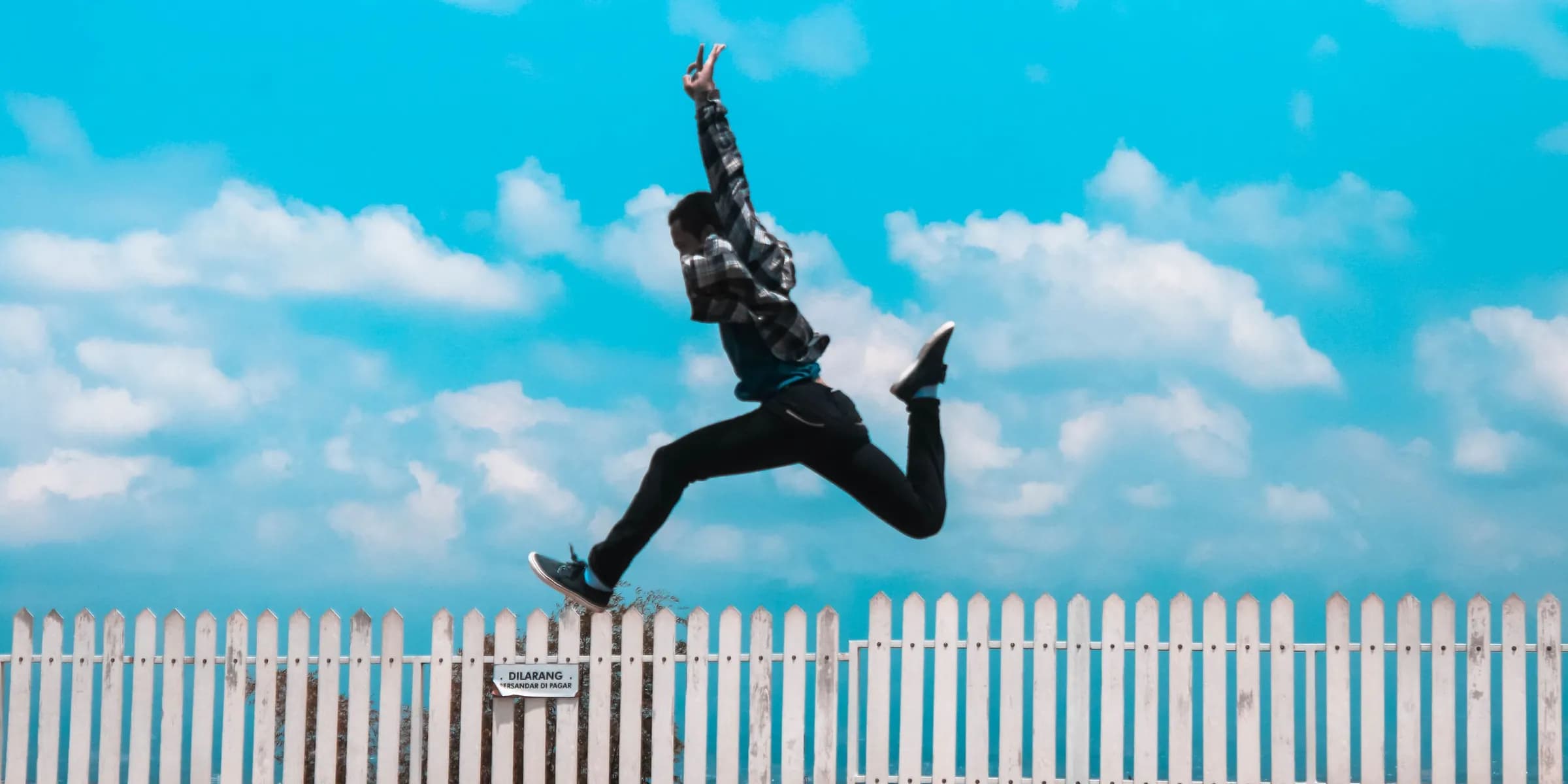 Homem saltando sobre uma cerca branca contra o céu azul