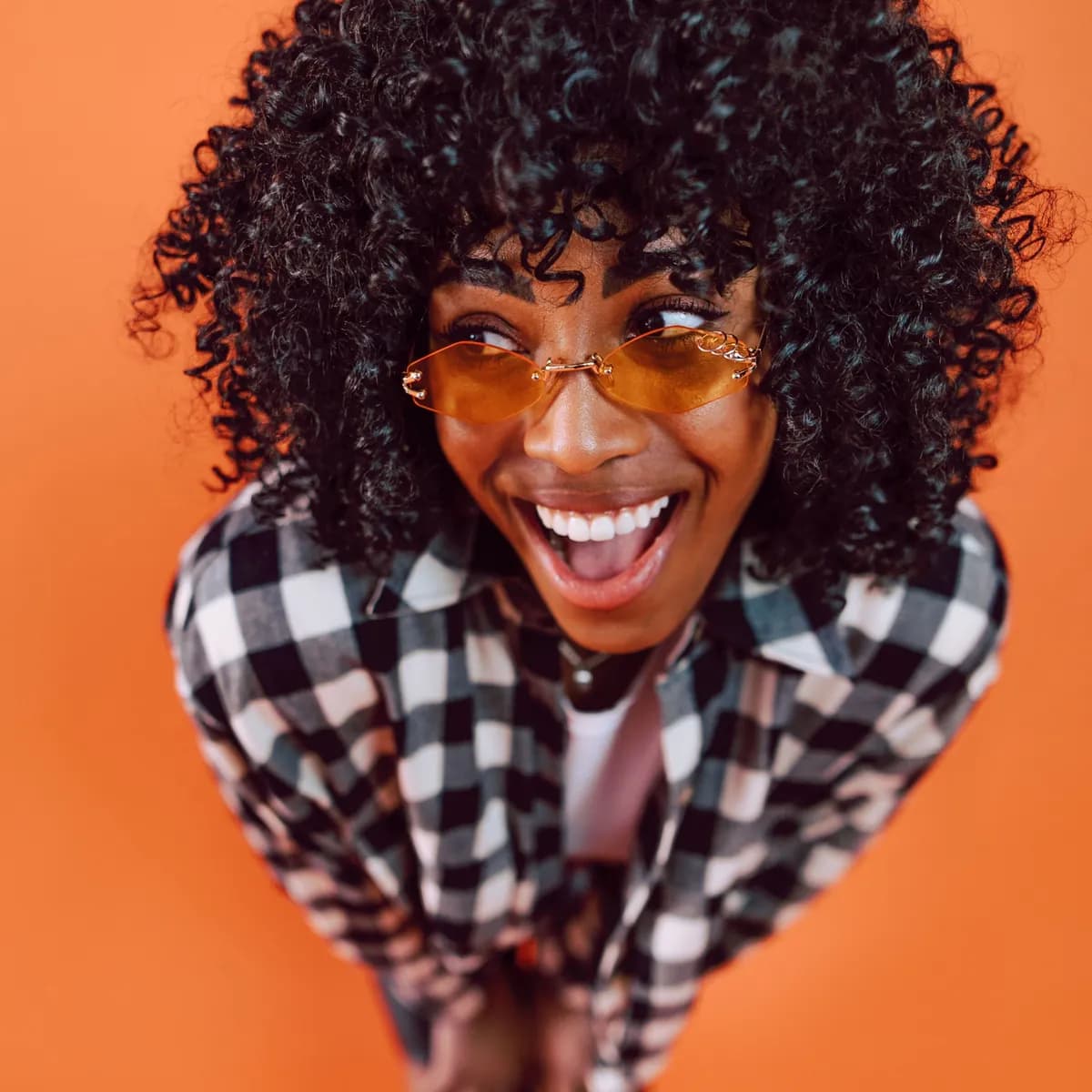 Mulher rindo de camisa xadrez sobre fundo laranja